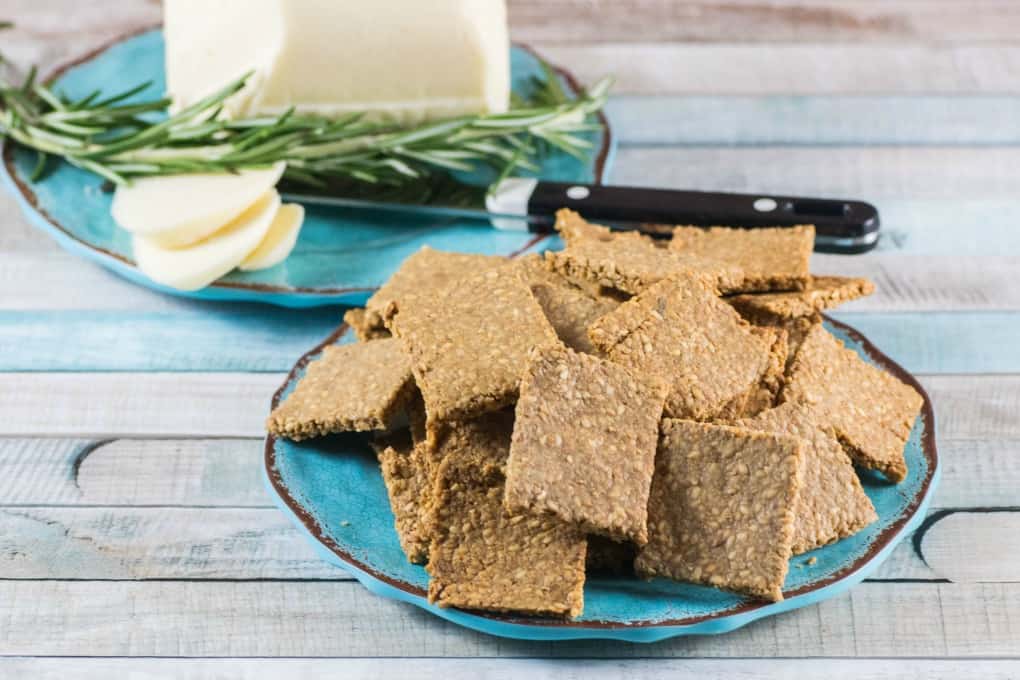 Gluten Free Crackers Recipe on a blue plate with sliced white cheese in the background. 