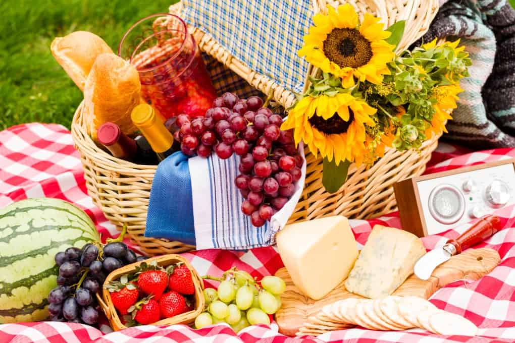 Picnic basket with food, fruit, wine, cheese, sunflowers overflowing onto a checkered table cloth