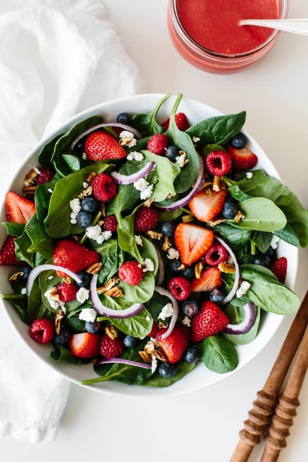Berry Spinach Salad in a white bowl with a jar of dressing and spoon