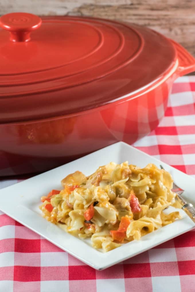 Cheesy Noodle Ham Casserole on a white plate on a checkered table cloth with a red casseorle