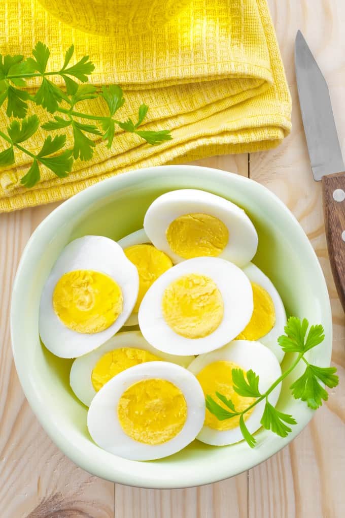 Halved hard boiled eggs in a bowl with parsley and a pretty yellow dish cloth