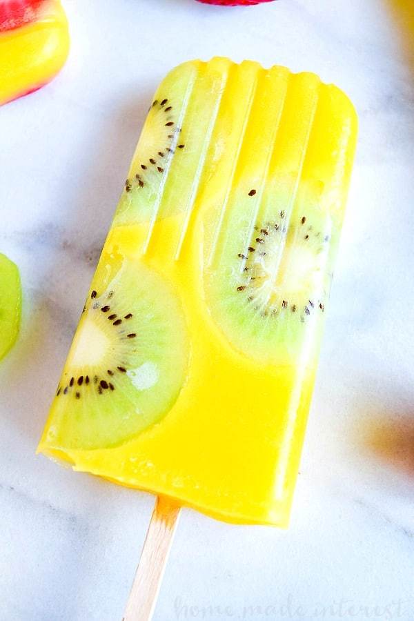 Mango popsicles with kiwi on a marble cutting board