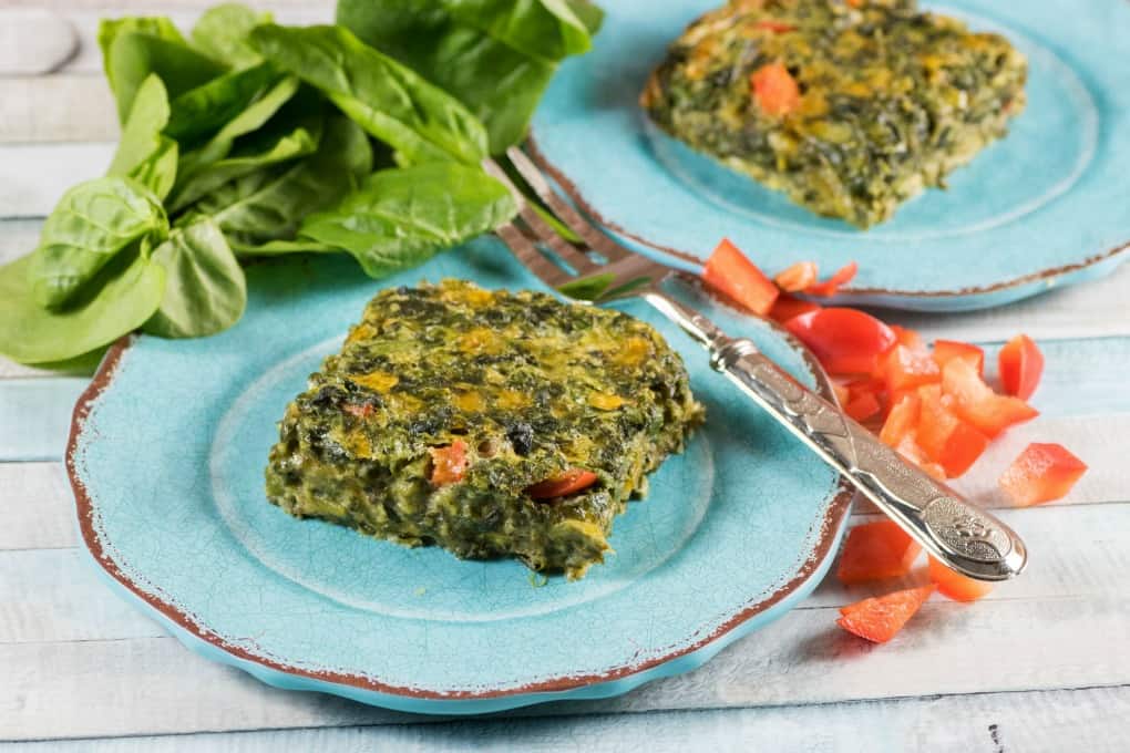 Spinach squares on blue plates with a fork, red pepper and spinach