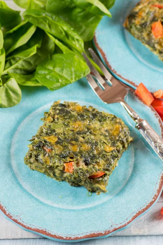 A Delicious Spinach Square on a blue plate with a fork and fresh spinach in the background