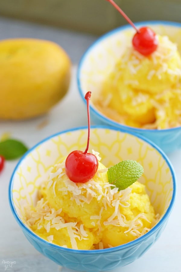 Mango pineapple sorbet in a blue bowl with coconut a cherry and a mint leaf on top