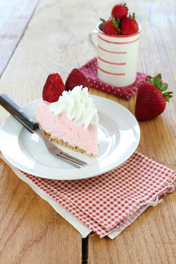 Slice of strawberry cheesecake ice cream on a white plate with a fork and red and white napkin with strawberries around