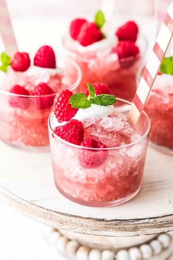 Raspberry Rose Granita in a small glass with raspberries, mint leaf and a spoon on a wooden board