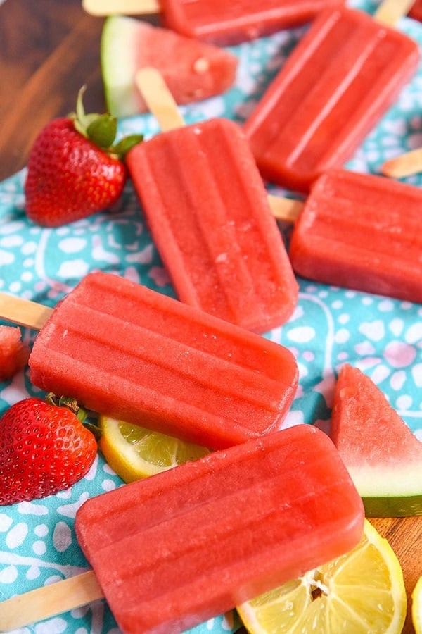 Strawberry watermelon popsicles on a blue cloth with strawberries and watermelon slices