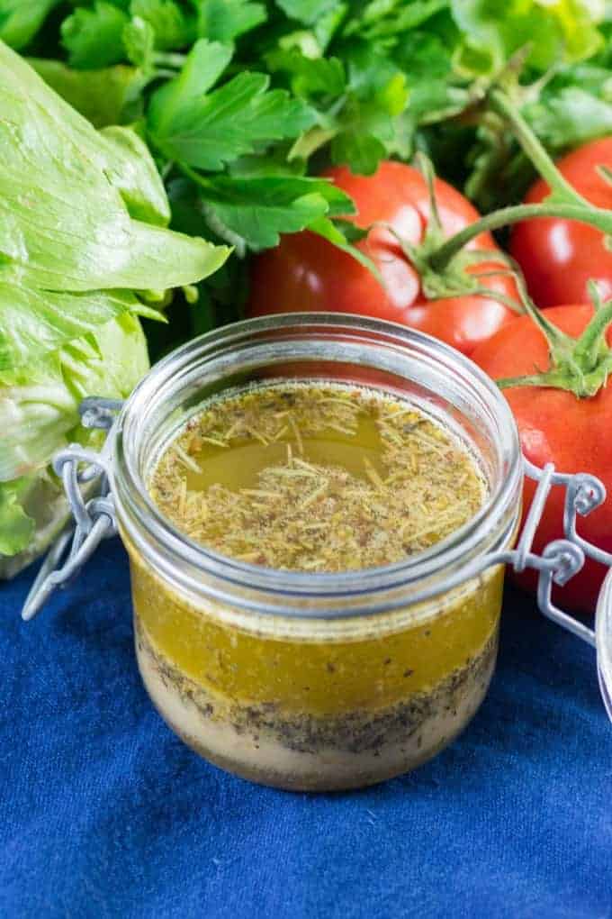 Homemade Italian Dressing in a small jar with tomatoes, lettuce and herbs