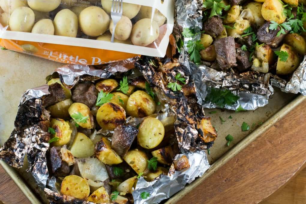 Bag of The Little Potato Company's Creamer potatoes lying down with foil packs on a baking sheet. 