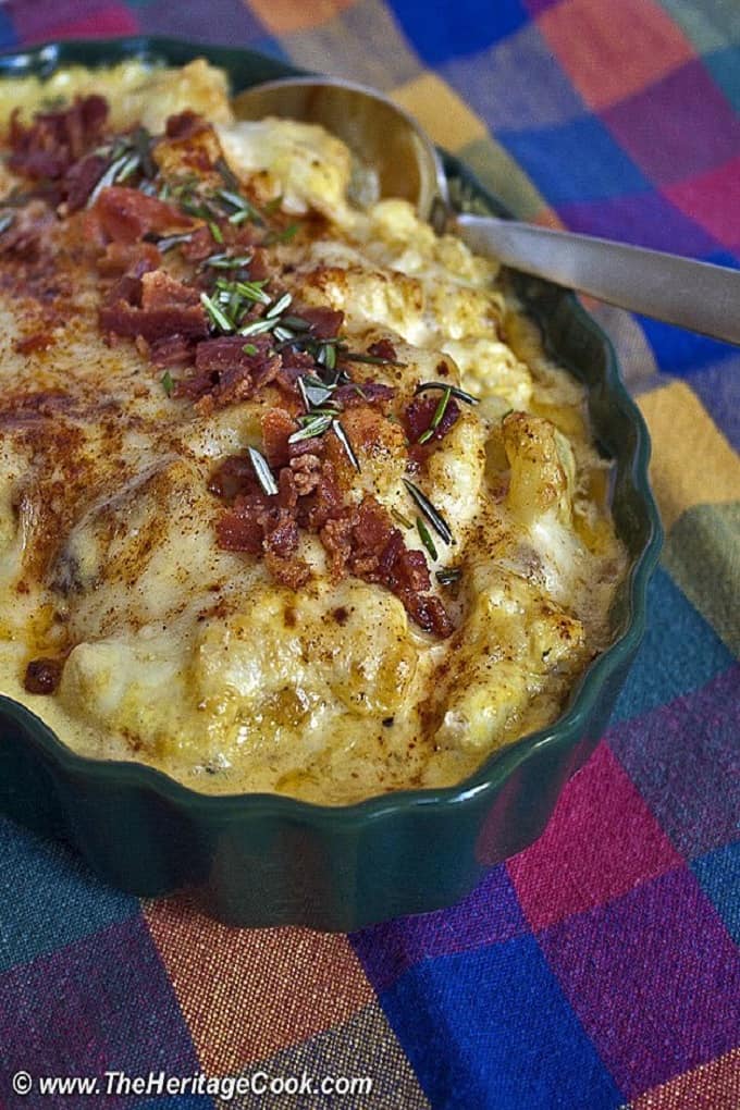 Cheesy Cauliflower Casserole in a dark green casserole dish and a metal spoon 