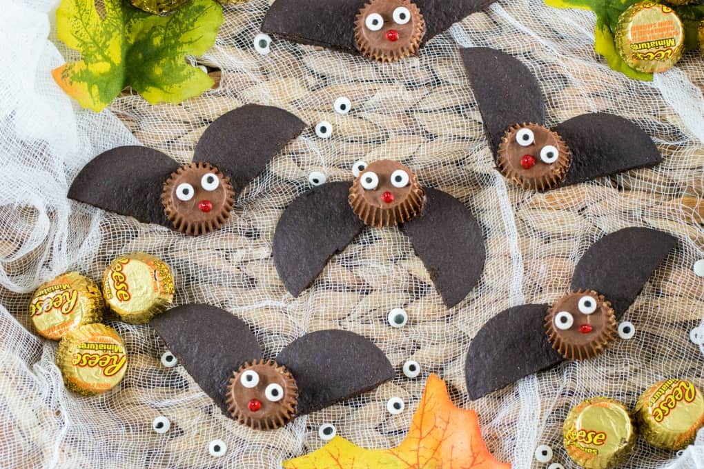 Easy Bat Peanut Butter Cups on a tray with cheesecloth and fall decorations of leaves, Reese's and eyeballs. 