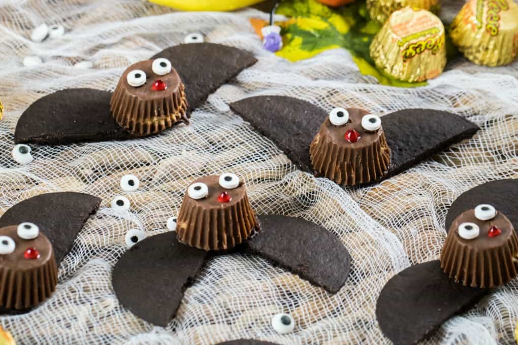 Easy Bat Peanut Butter Cups on a tray with cheesecloth and fall decorations of leaves, Reese's and eyeballs. 