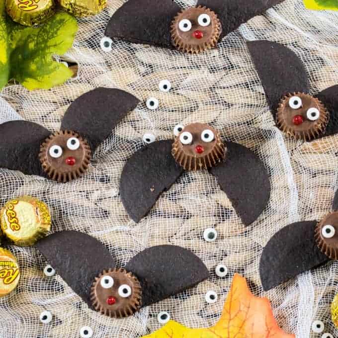 Easy Bat Peanut Butter Cups on a tray with cheesecloth and fall decorations of leaves, Reese's and eyeballs. 