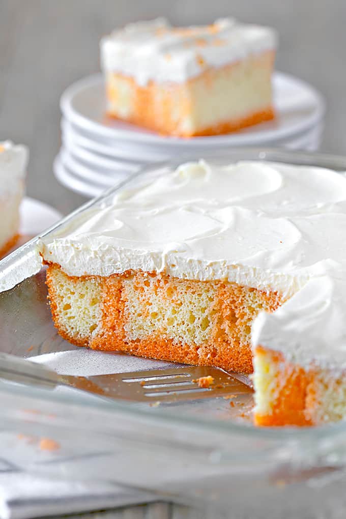 Orange Creamsicle Poke Cake in a cake pan with a slice on plates in the background