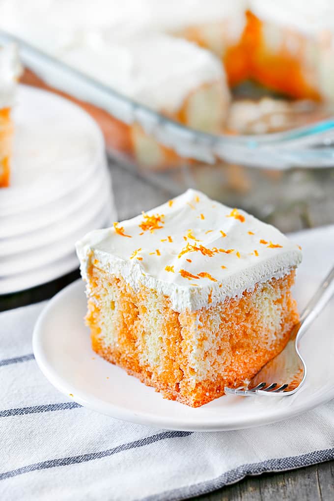 Close up of a slice of Orange Creamsicle Poke Cake on a white plate with a fork