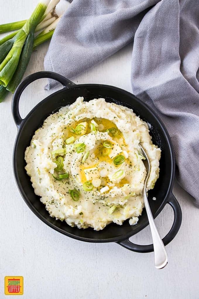 Irish Mashed Potatoes in a cast iron pot on a white table cloth with a silver serving spoon