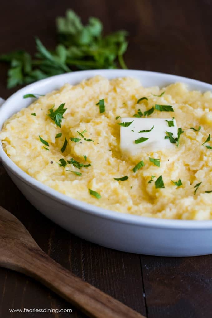 Mashed rutabaga in a white bowl with a pat of butter and a wooden serving sppon