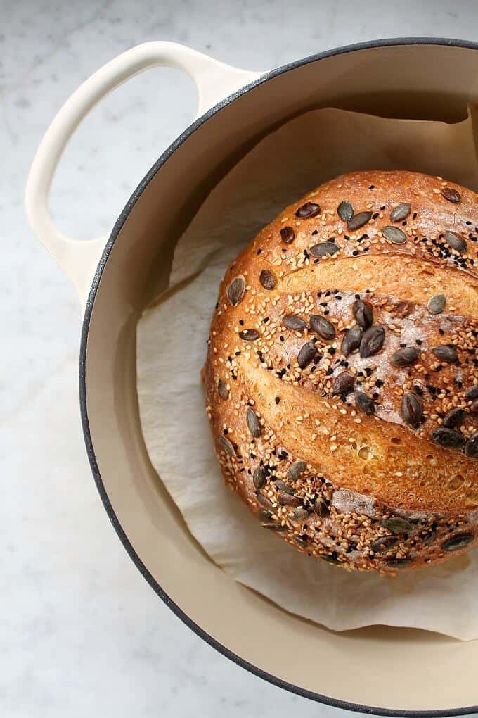 Pumpkin No Knead Bread - Bread boule topped with various seeds siting in an off white Dutch oven.