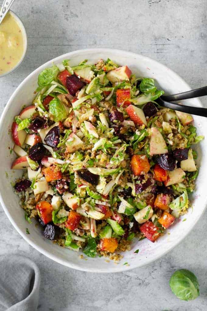 Fall harvest salad in a white bowl with black serving spoons