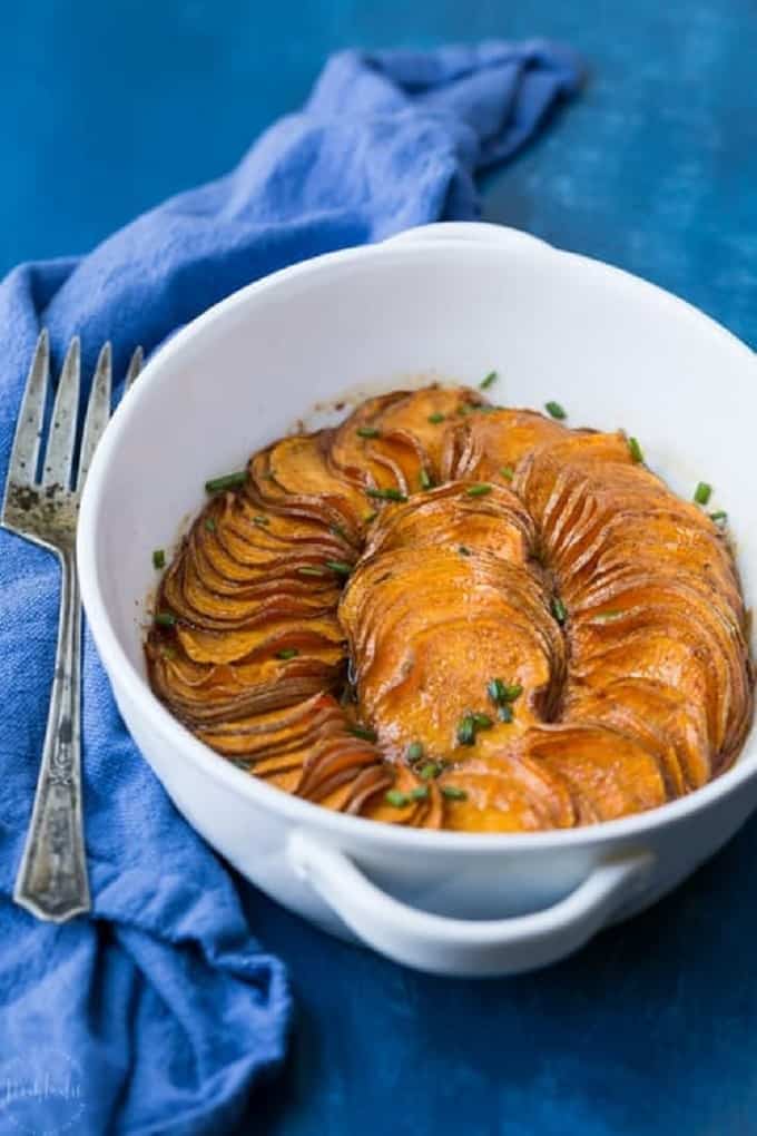 Scalloped sweet potatoes in a white oval dish on a blue table cloth and serving fork