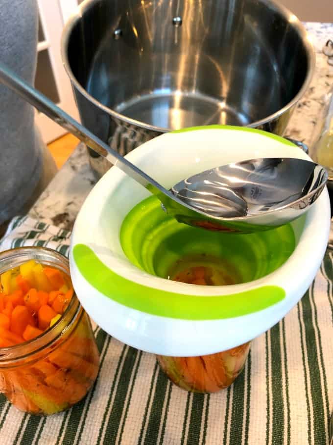 Using a funnel to pour brine into jars of carrots.