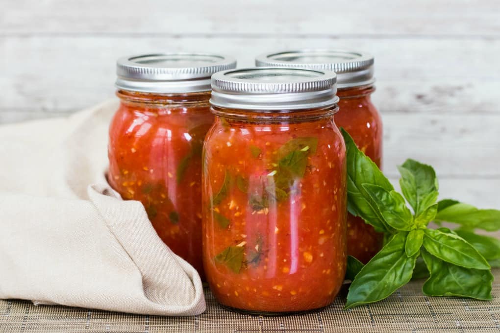 Jars of Pomodoro sauce with fresh basil and a tea towel. 