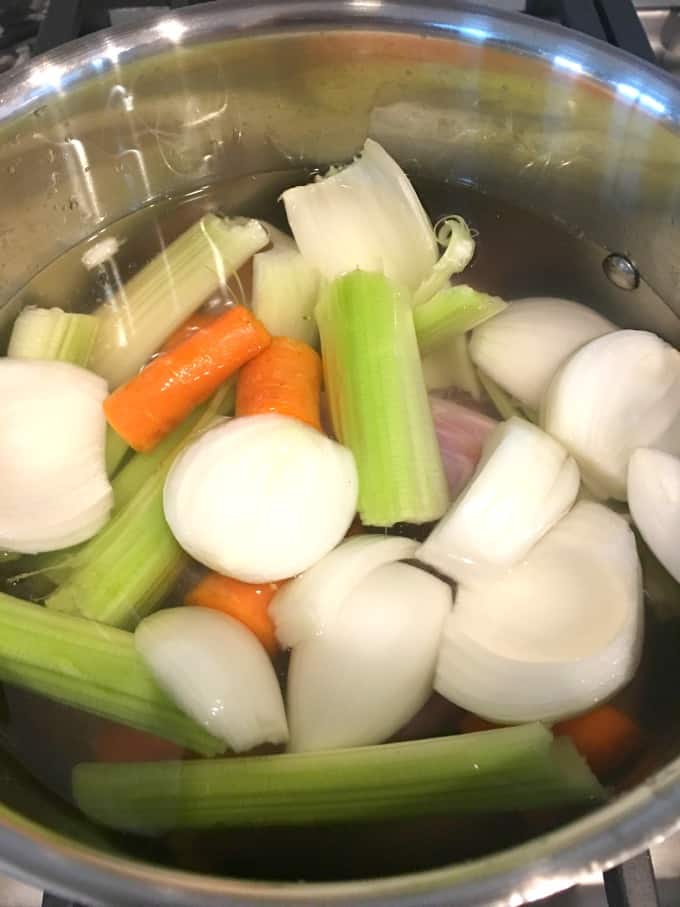 Turkey neck and giblets with carrots, onions and celery in water in a pot.