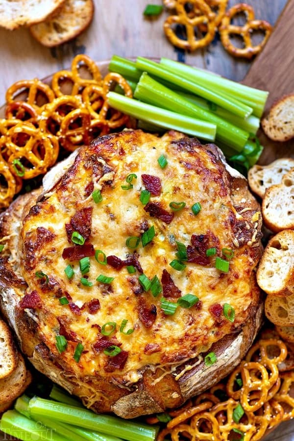 Baked Bacon Cheese Dip inside a loaf of bread with pretzels, crostinis and celery from 18 Easy Hot Party Appetizer Recipes
