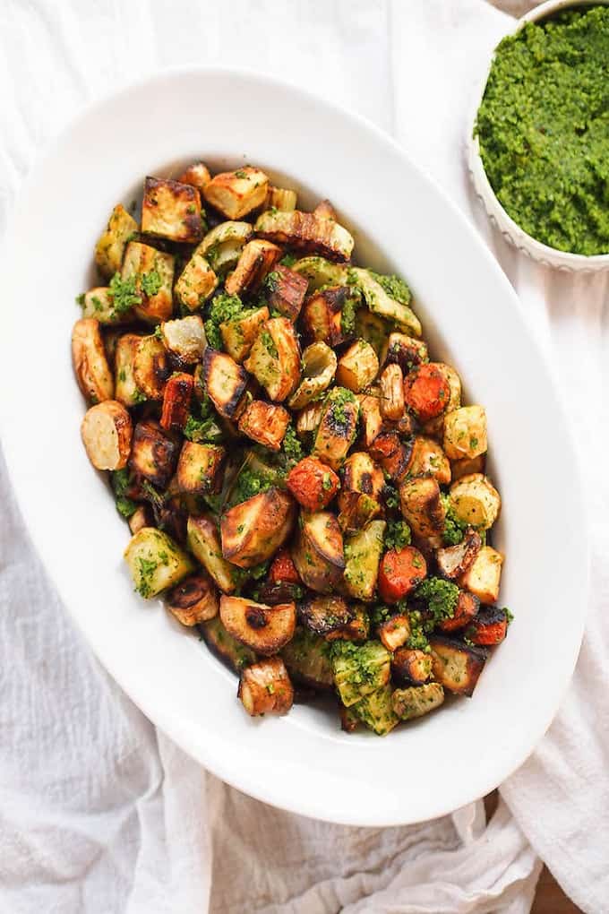 Roasted fall vegetables with kale hazelnut pesto in a white serving bowl on a white table cloth