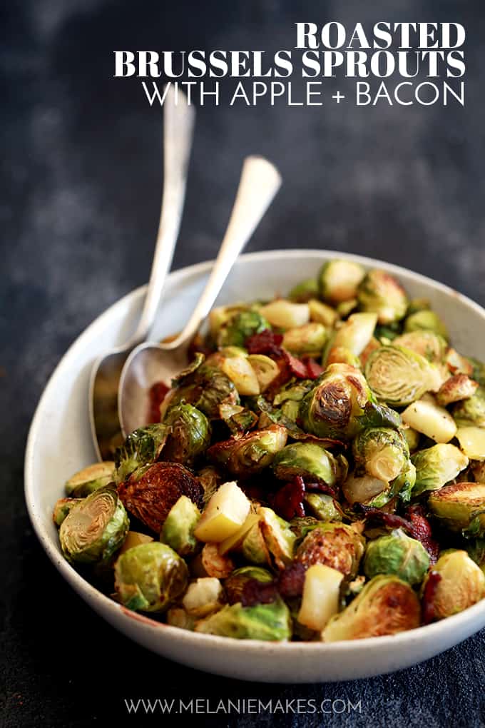 Roasted Brussel sprouts with apple and bacon in a white serving bowl with 2 silver serving spoons 