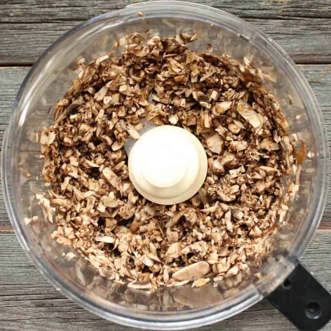 Chopped mushroom sit in the bowl of a food processor.