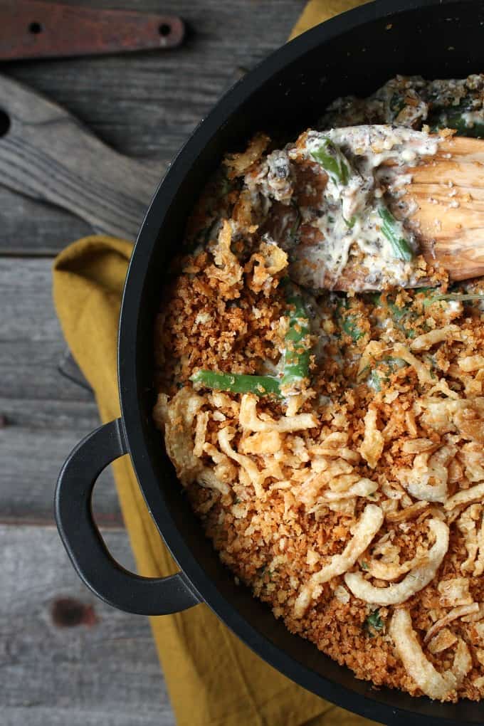 Zesty Green Bean Casserole - An overhead shot of a golden crumb and onion topped casserole with wooden spoon in a black baking dish.