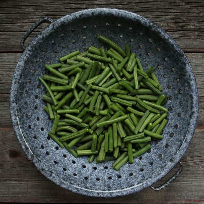 Bright green beans sit in a old fashioned grey colander.