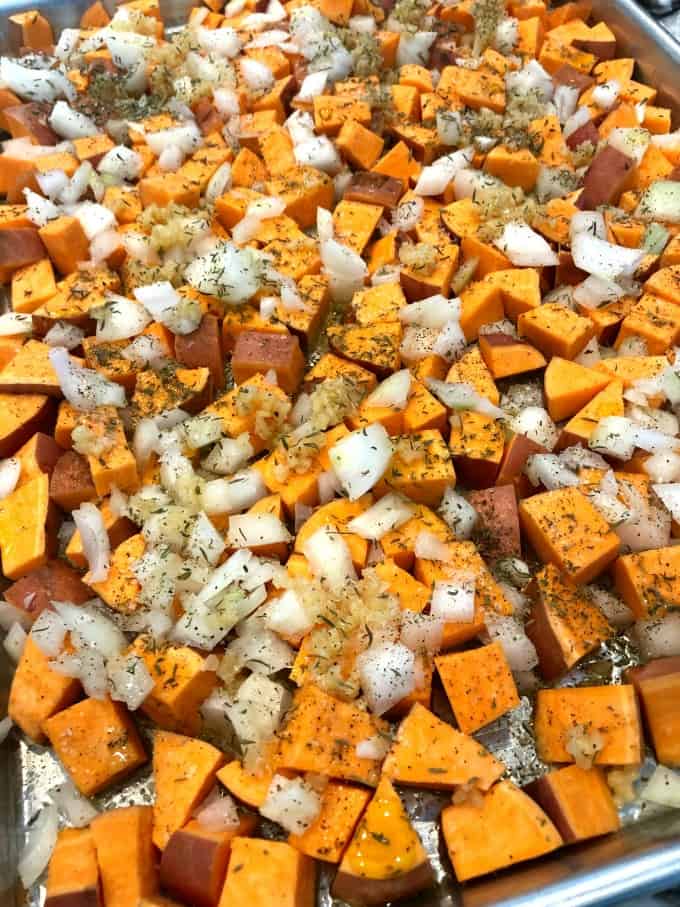 Sweet potatoes, onions, garlic with thyme, salt and pepper on a sheet pan