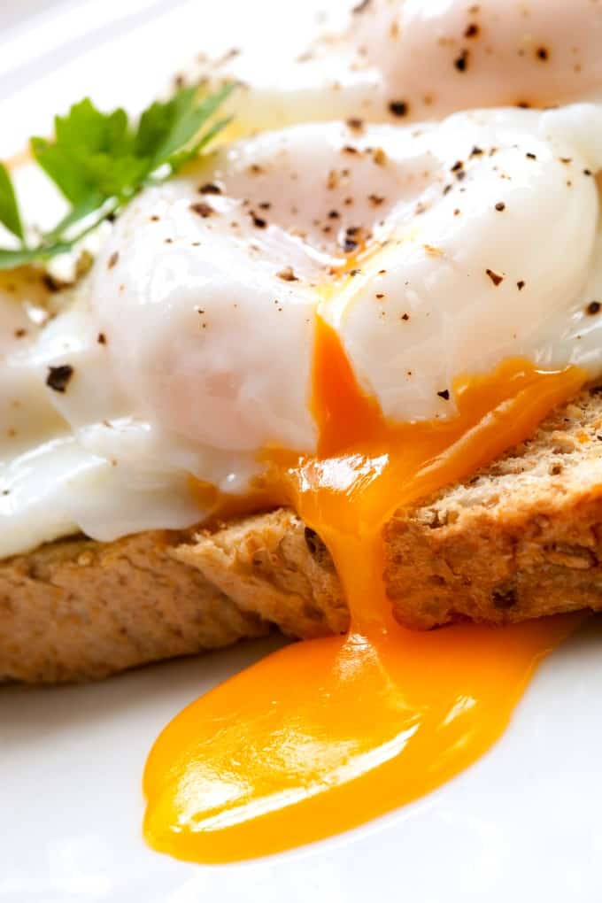 A perfectly poached egg on toast oozing onto a white plate. 