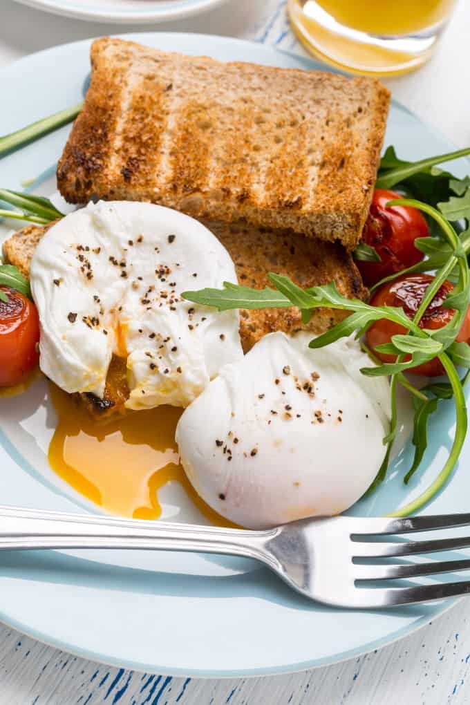 Poached eggs over toast on a blue plate with arugula and blistered tomatoes