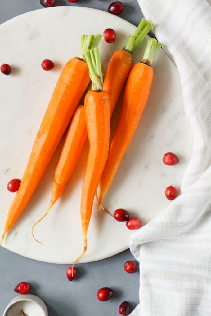 3 carrots on a marble tray with cranberries