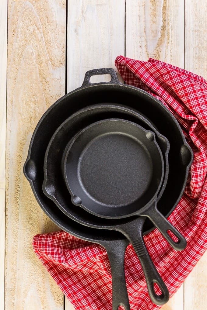 Cast Iron fry pans inside each other with a red check towel on a wooden board