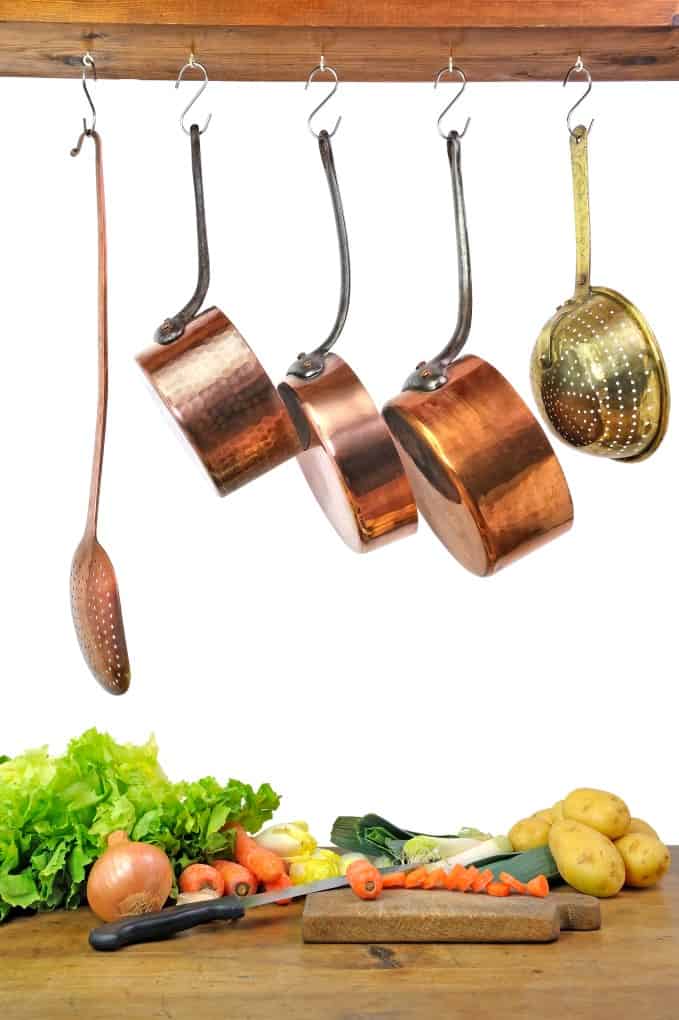 Copper pans and ladles hanging about vegetables on a cutting board. 