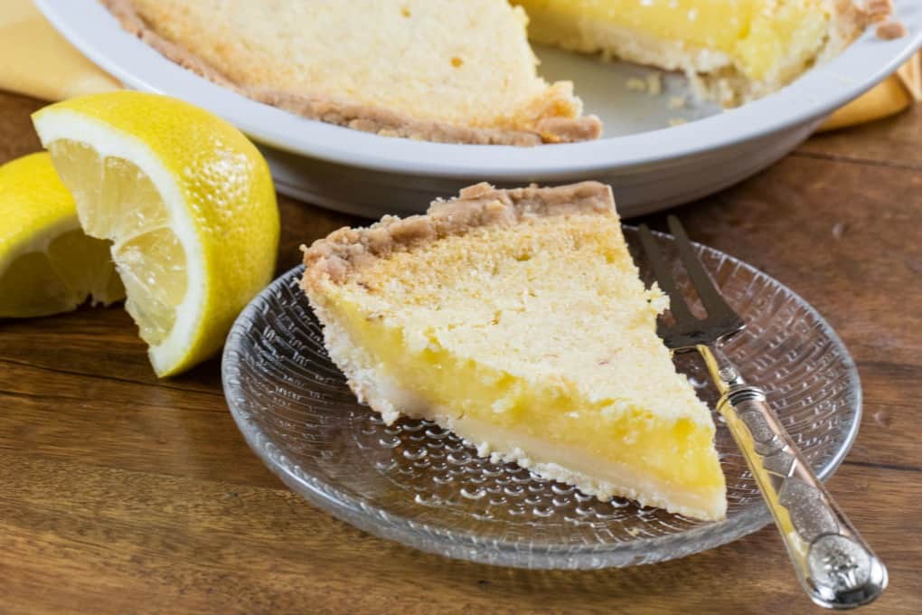 Lemon Chess Pie on a glass dish with a fork and the pie in the background