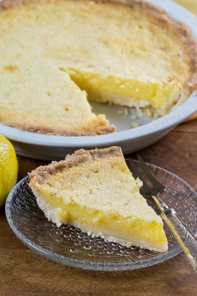 Slice of Lemon Chess Pie on a small glass plate with a fork and the pie in the background