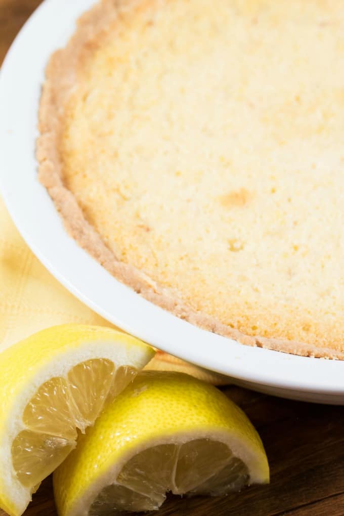 Lemon Chess Pie in a white pie dish with lemons in the forefront