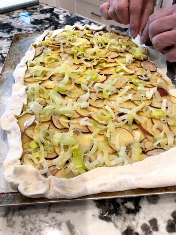 Folding up the edges of a potato galette with leeks on top