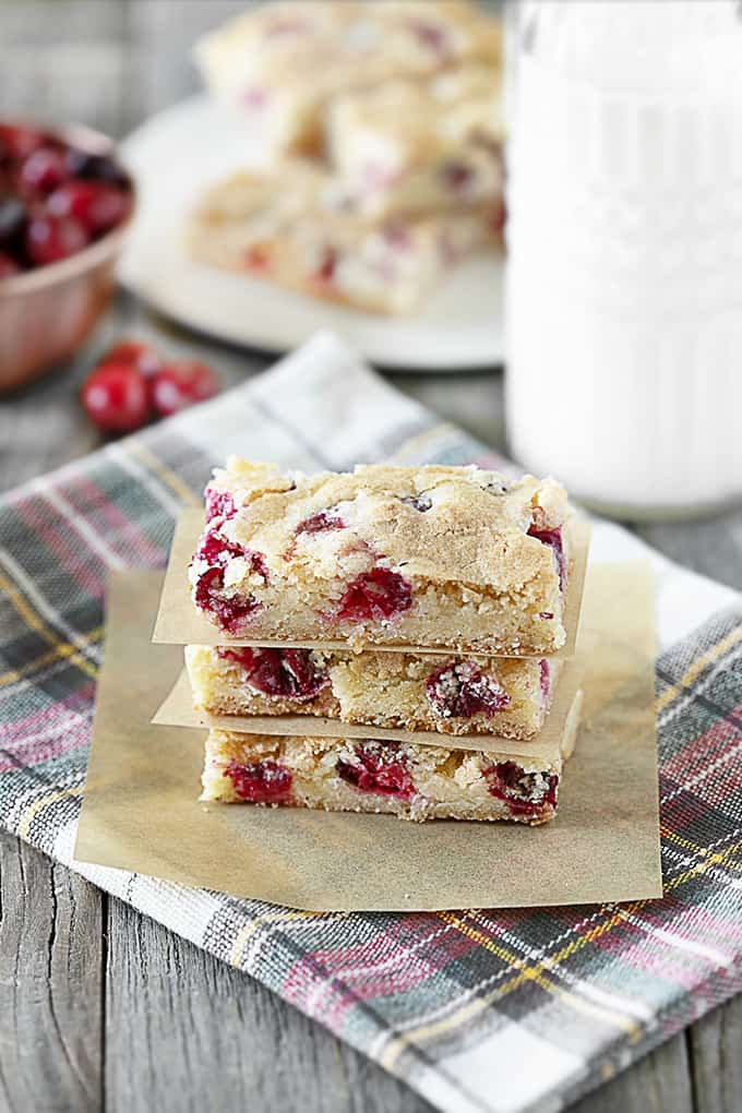 Cranberry bars stacked with parchment paper between on a plaid tea towel