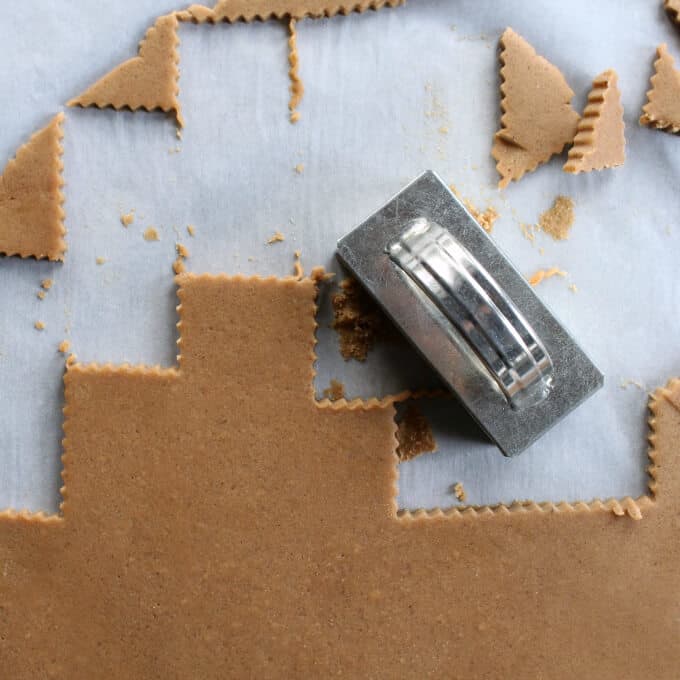 Brown dough is rolled out on a white parchment paper as a few rectangular cookies are cut out.