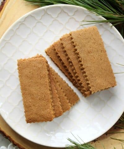 Speculoos Cookies (Classic Recipe)-A white textured plate filled with sparkling brown rectangular cookies surrounded by evergeen branches.