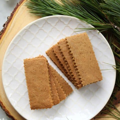 Speculoos Cookies (Classic Recipe)-A white textured plate filled with sparkling brown rectangular cookies surrounded by evergeen branches.