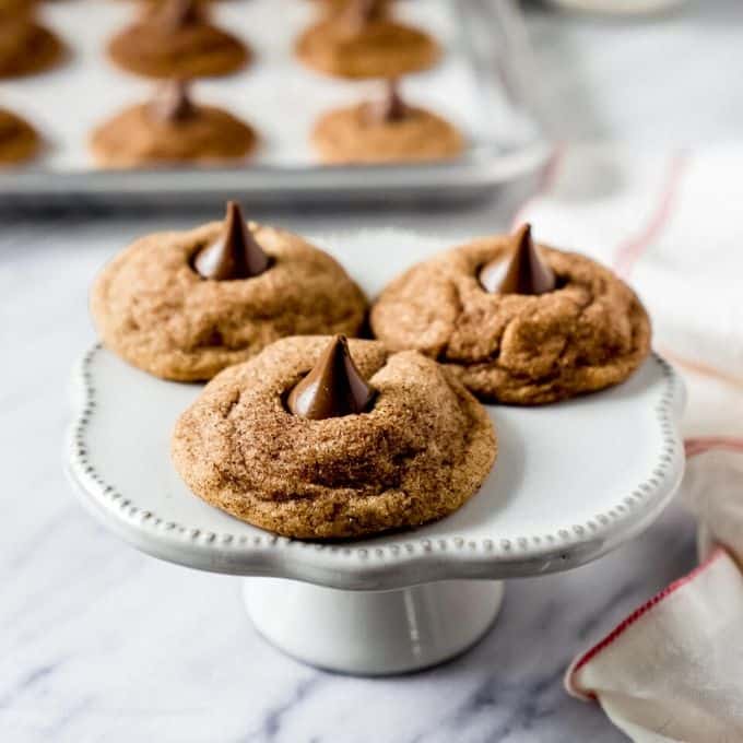Easy Snickerdoodle Hershey Kiss Cookies on white platter with others in the background on a cookie sheet