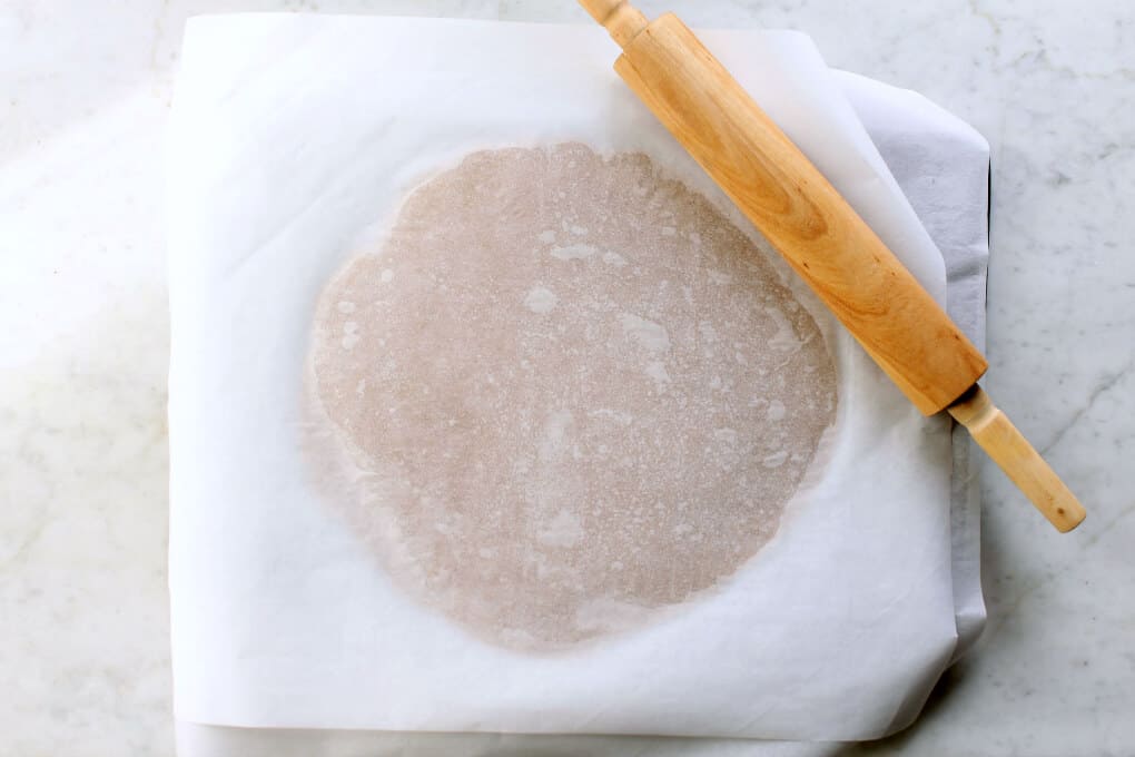 Brown cookie dough is visible through parchment paper as a rolling pin lays nearby.